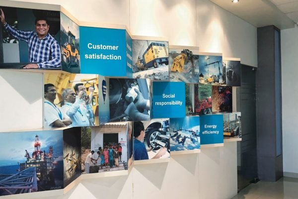 Corporate office branding wall featuring cube installations showcasing customer satisfaction, social responsibility, and energy efficiency through industrial and workplace visuals.