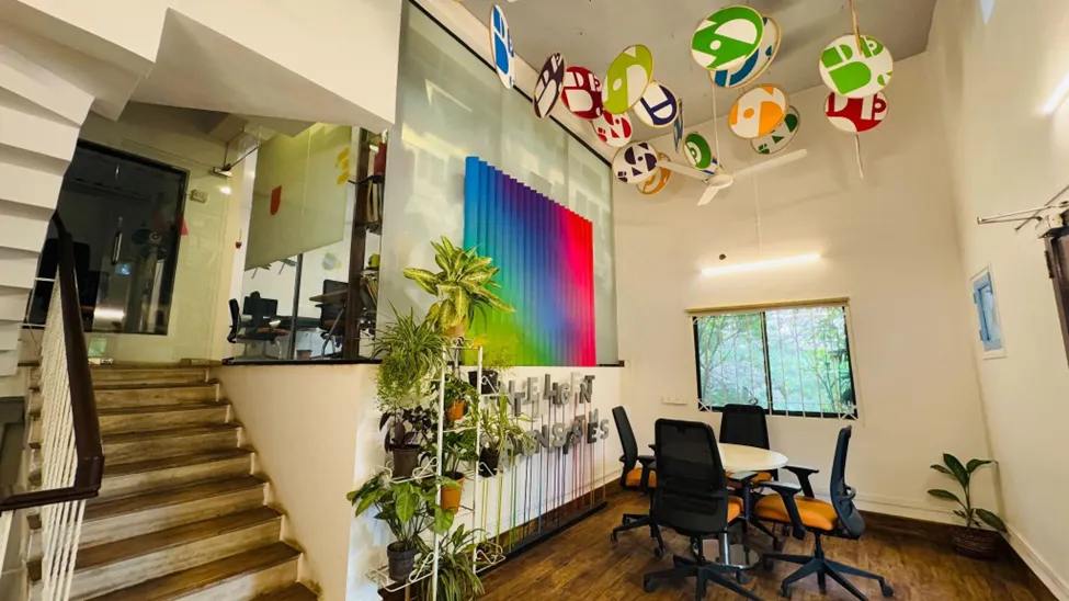 Creative office interior with colorful wall art, indoor plants, staircase, and collaborative workspace by Interics Designs