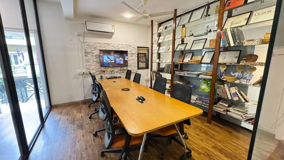 Modern office conference room with wooden meeting table, glass bookshelf display, and collaborative workspace design